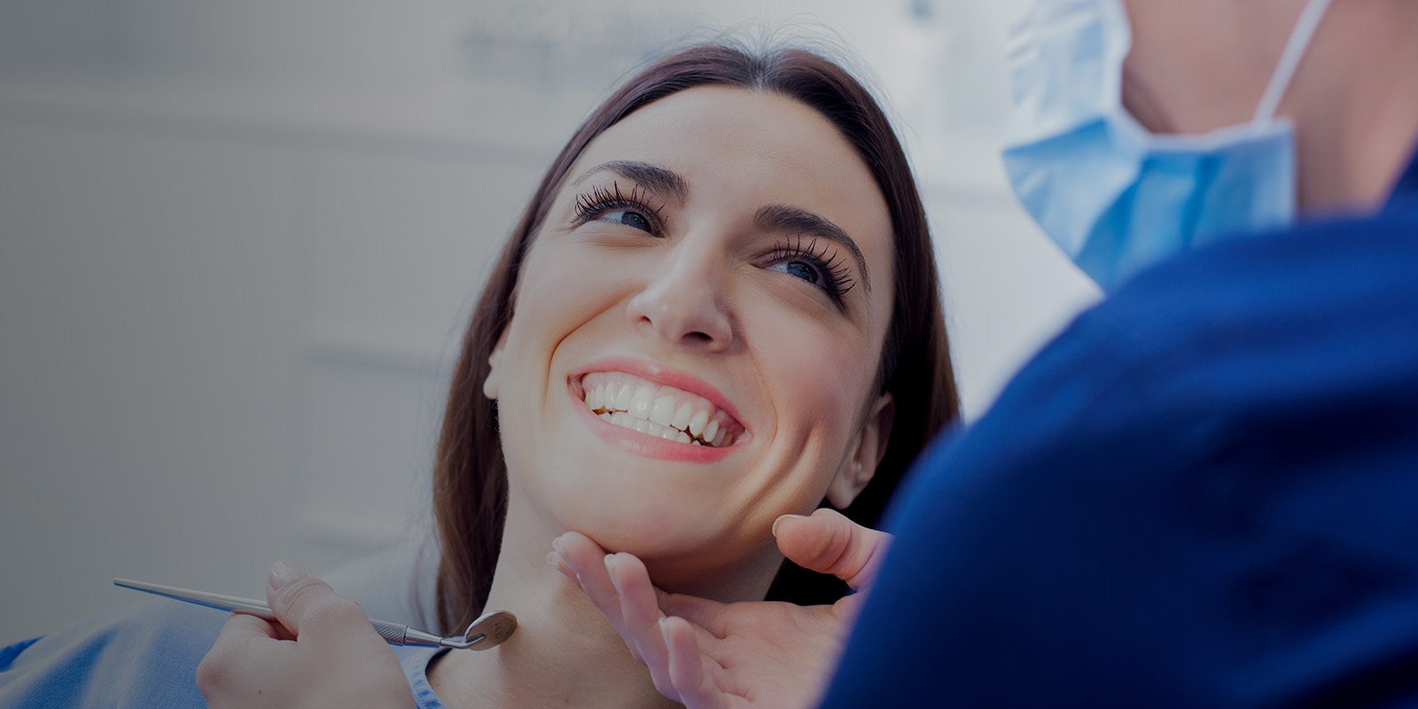 A woman smiling while a dentist checks her teeth.