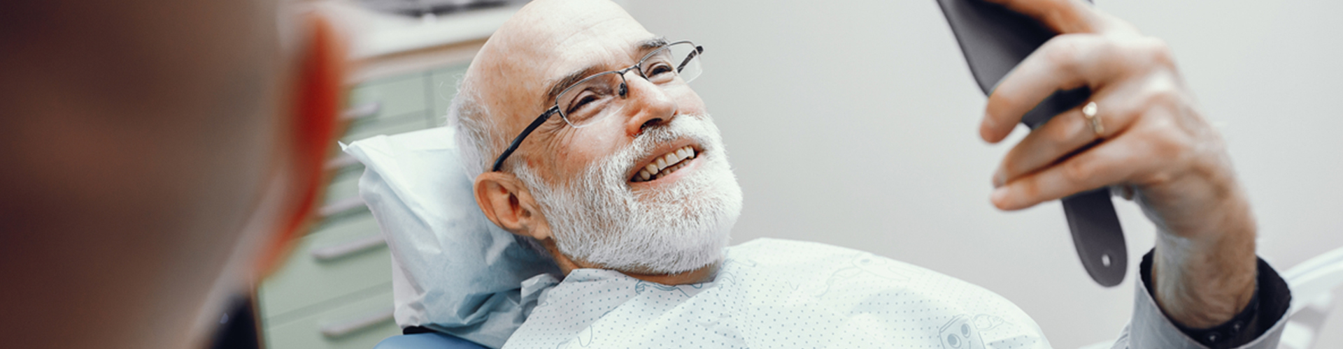 male sitting in dental chair admiring smile in mirror
