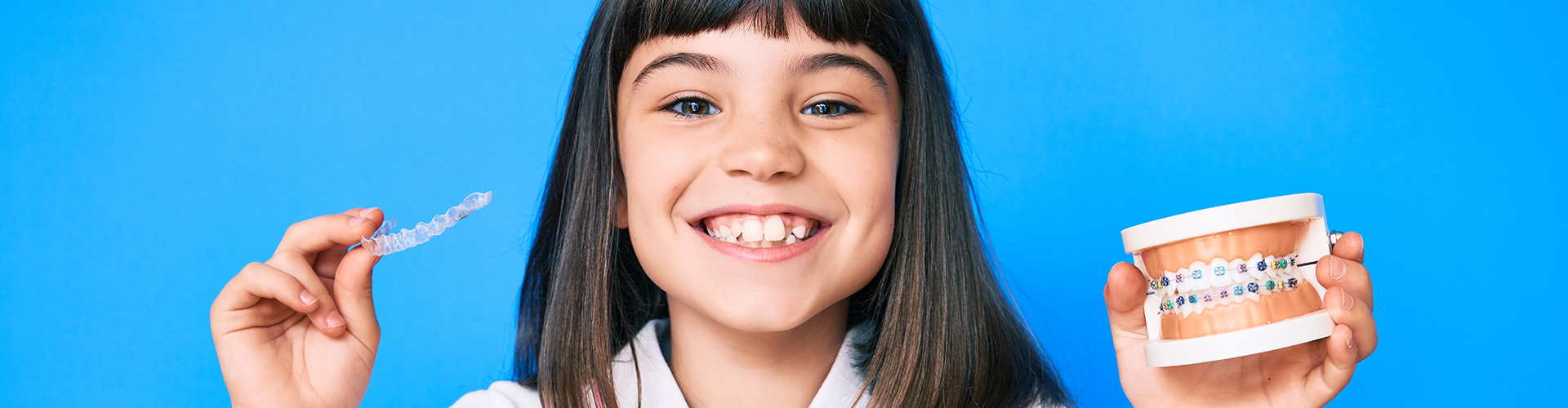girl holding clear aligner in one hand and teeth model with braces in the other