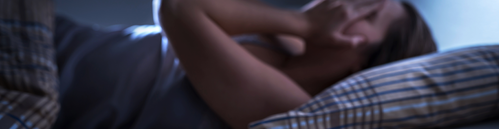 woman laying in bed covering face with hands with alarm clock in foreground