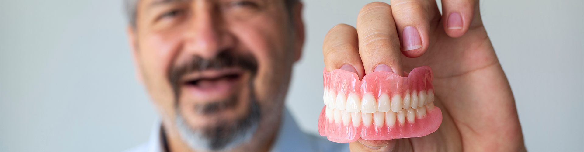Toothless smiling man holding dentures.