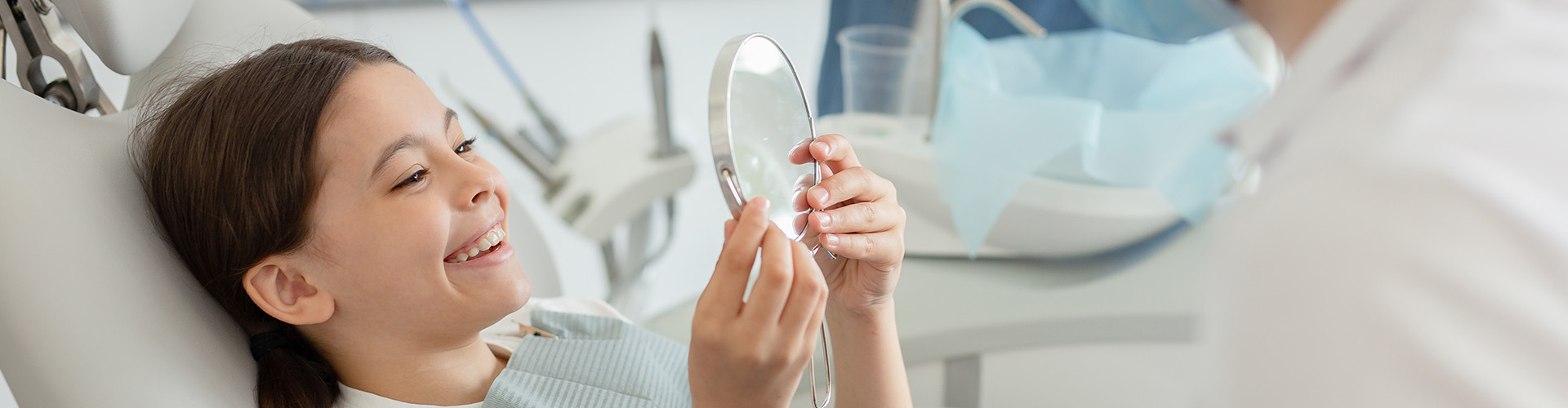 child in dental chair smiling into hand mirror