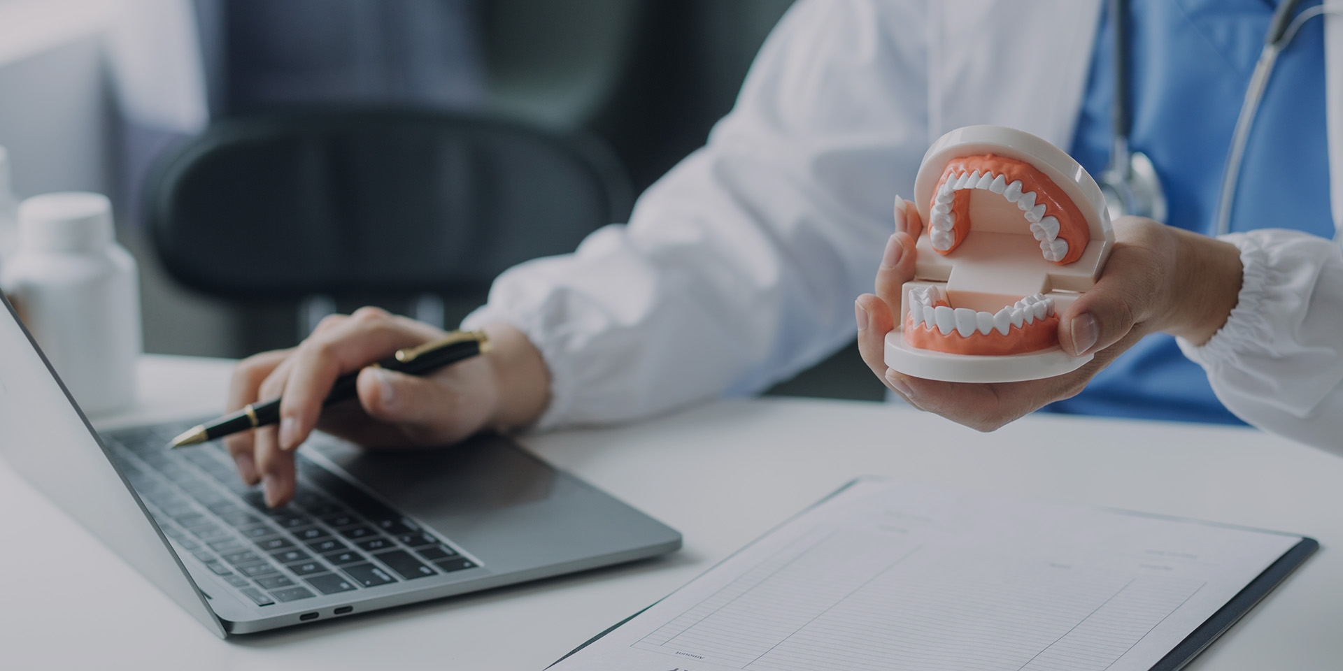 A dentist typing on a laptop while holding a denture model.