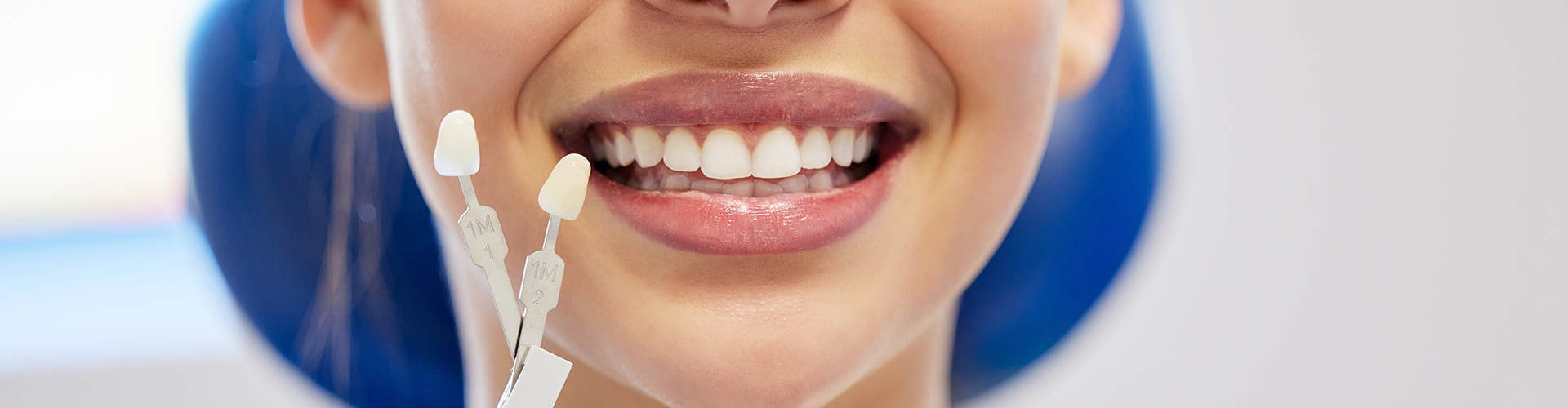 gloved hand holding shade-matching tool next to woman's smile