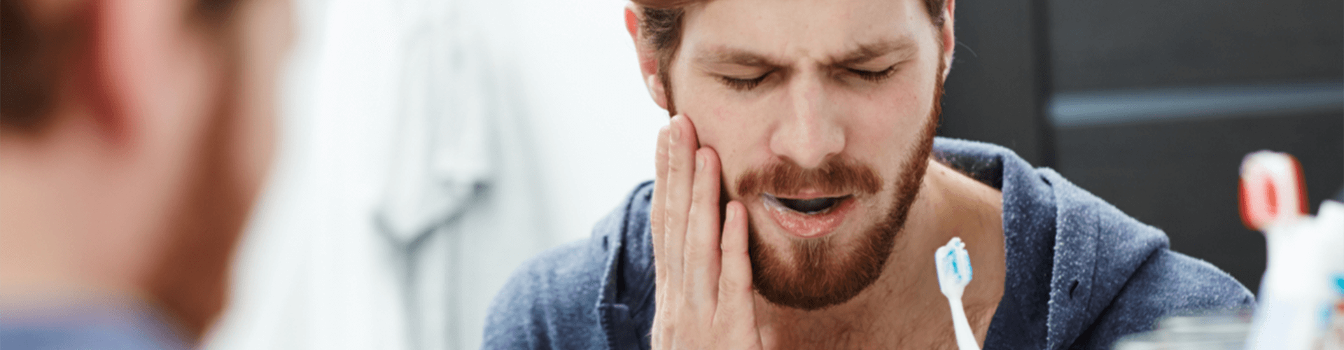 Man holding cheek in pain while brushing teeth.