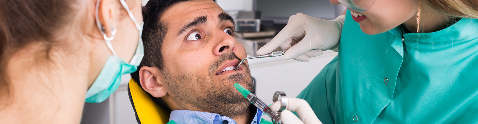 dentists using dental tools on anxious man in dental chair