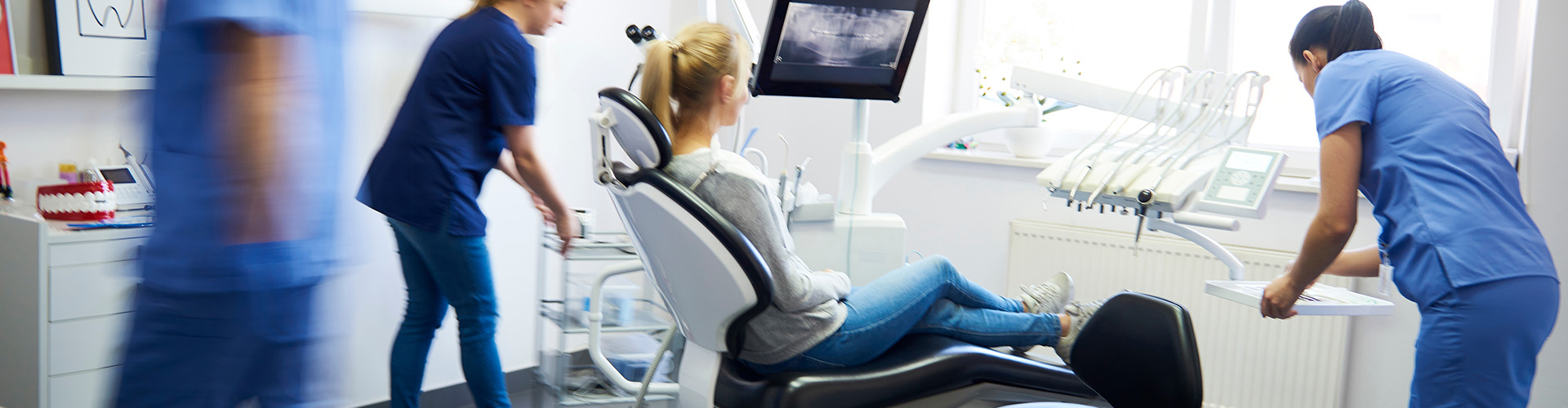 woman sitting in a dental chair while dental stuff move around her