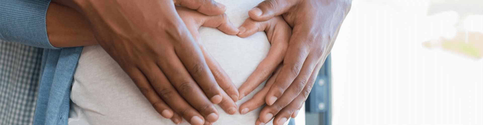 Couple's hands forming a heart on a pregnant belly.
