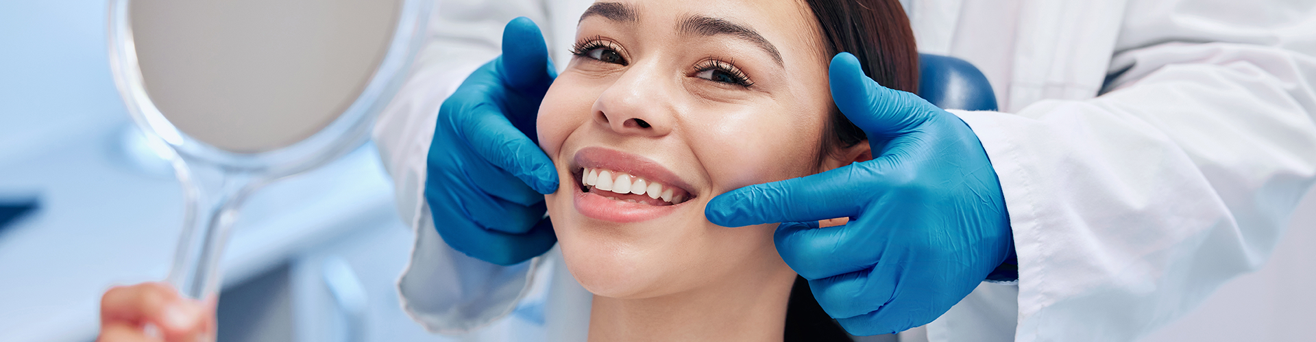 patient smiling into hand mirror while gloved hands point to her smile