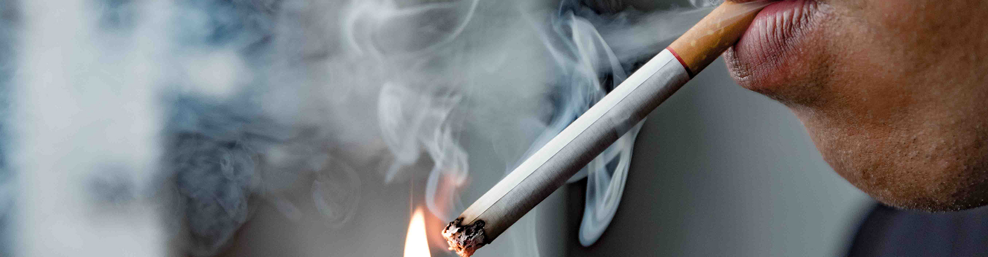 Man lighting a cigarette between his lips.