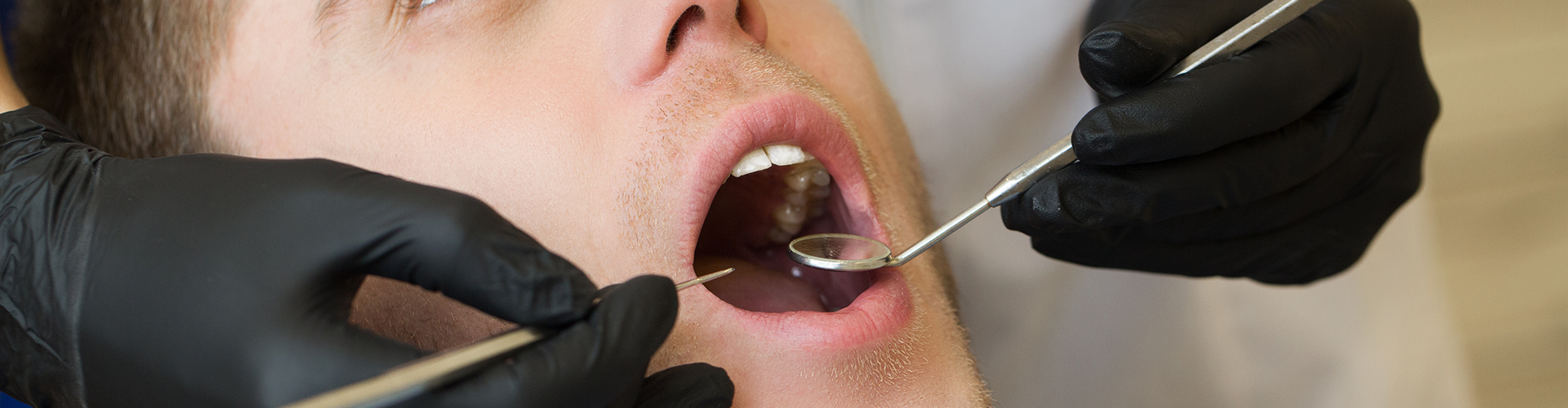 dentist holding dental tools in man's open mouth