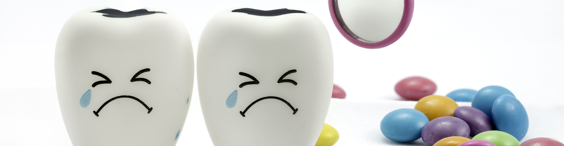 Model of two frowning teeth with cavities next to candy and a dental mirror.