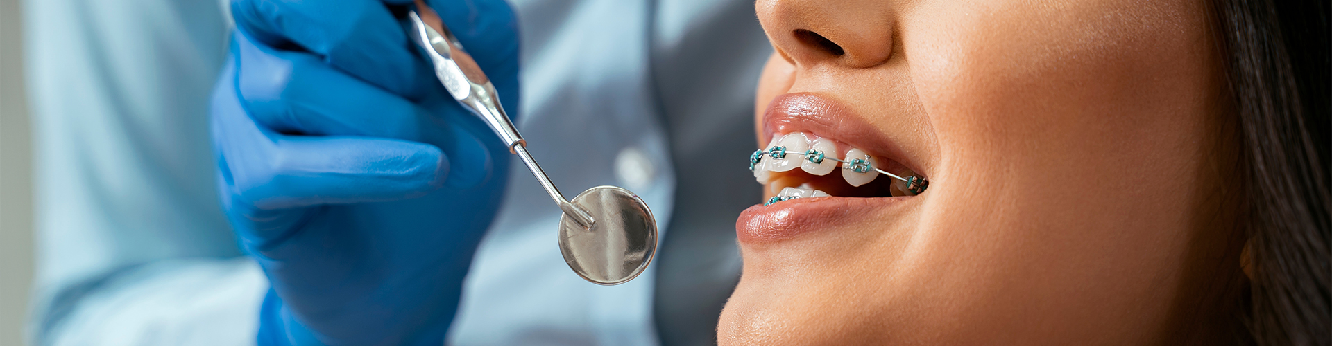 Dentist holding a dental mirror by a smiling woman wearing braces.