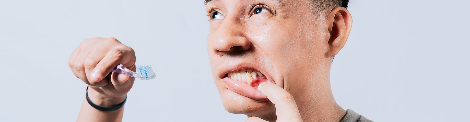 man holding toothbrush and pulling down lip to show gums