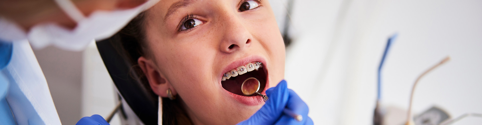 dentist holding mirror in mouth of chil wearing braces