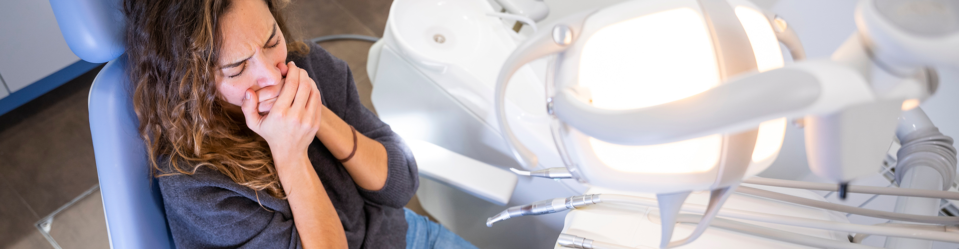woman in a dental chair covering her mouth with both hands
