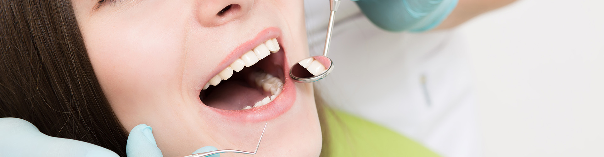 Close-up of a woman with her mouth open being examined with a dental mirror.