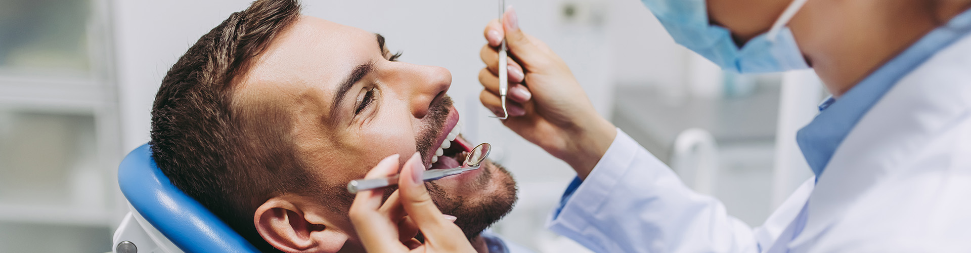 dentist with dental tools looking in man's mouth