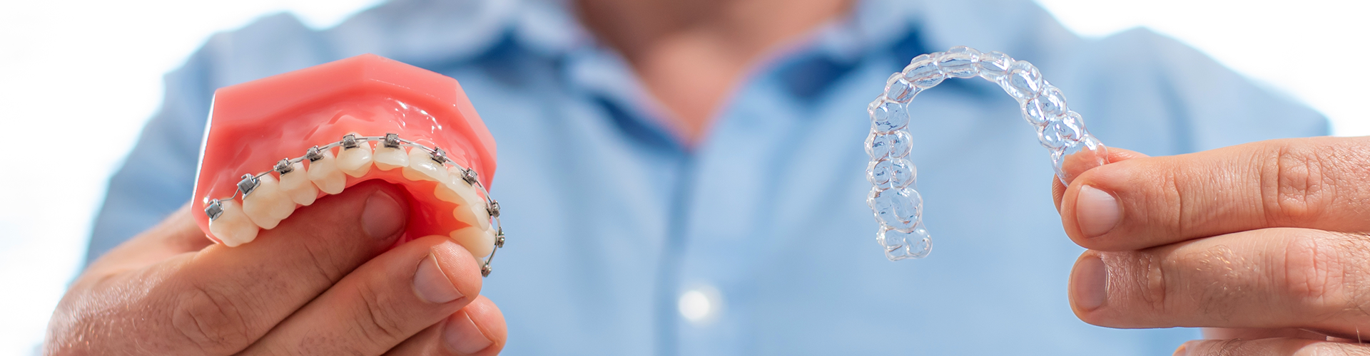 man holding braces in one hand and aligner in the other