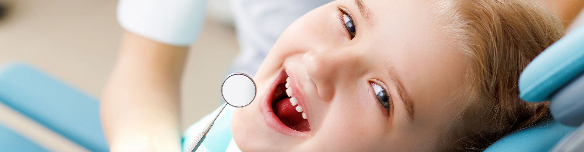 dentist holding a dental mirror beside girl's mouth