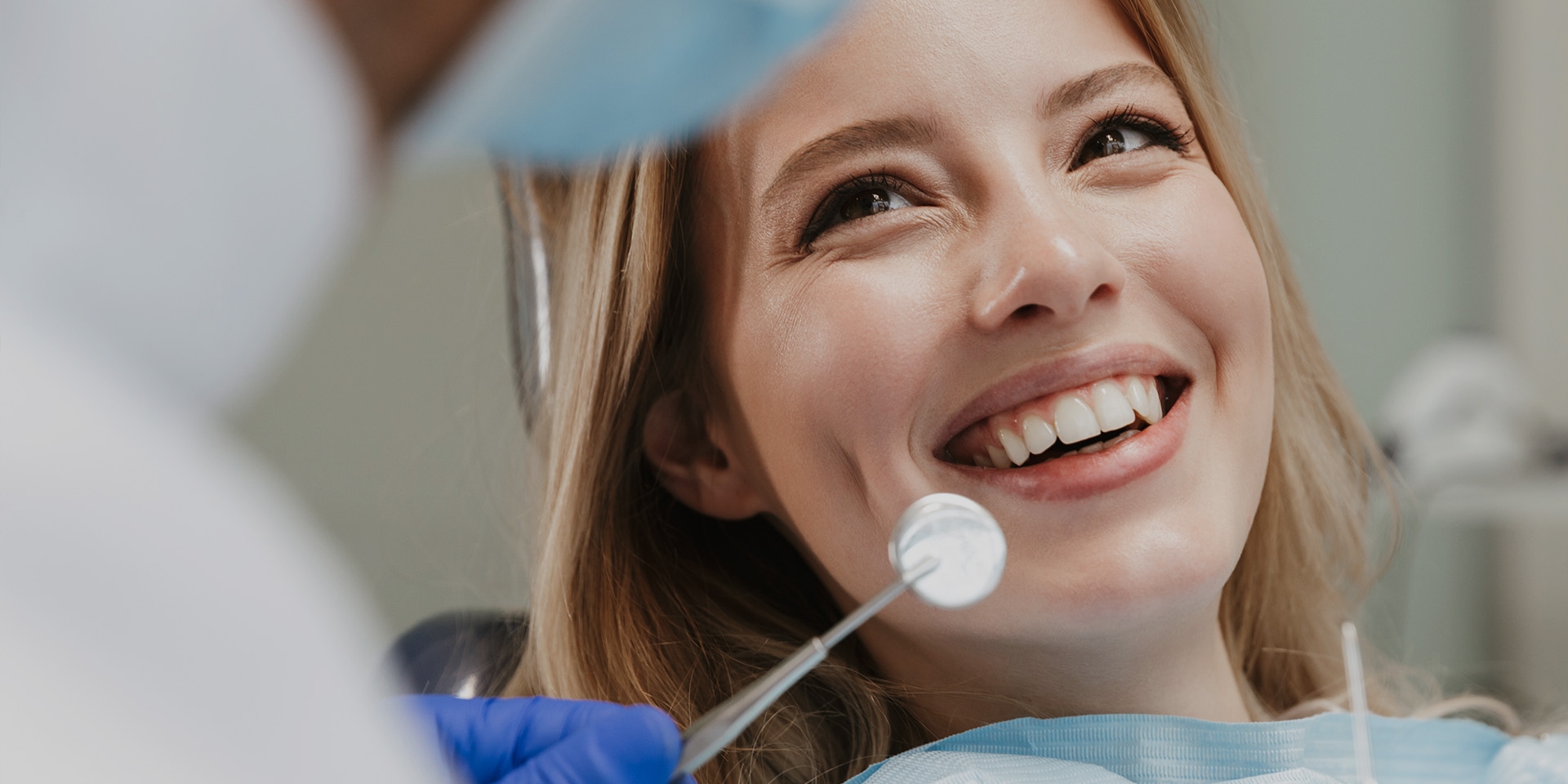 A woman smiling with a dental mirror held in front of her teeth.