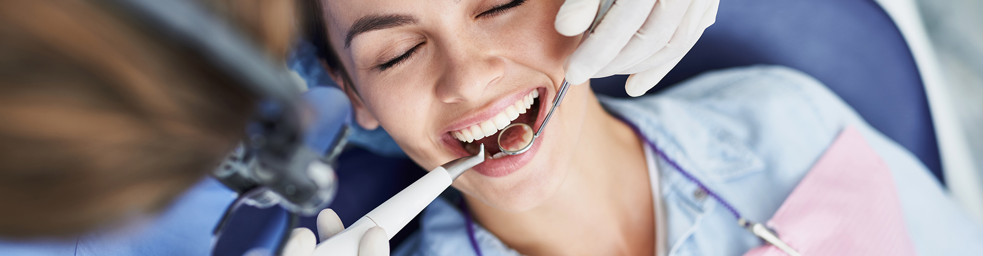 Dentist putting dental tools into a woman's mouth.