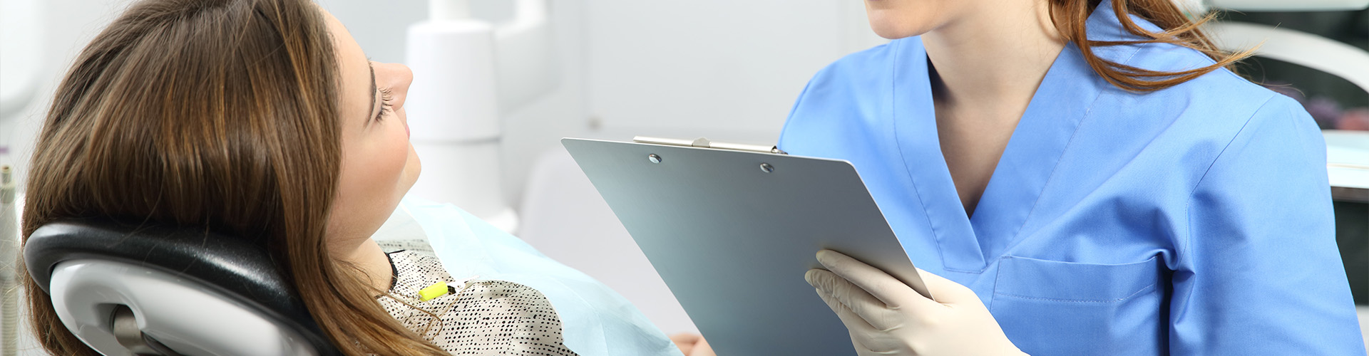 A patient in the dentist chair while the dentist explains something, holding a paper board.