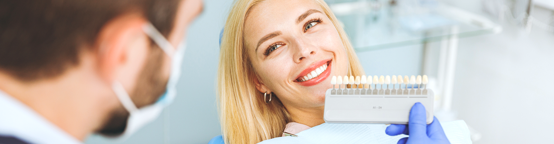 dentist holding tooth-shade-matching tool against woman's smile