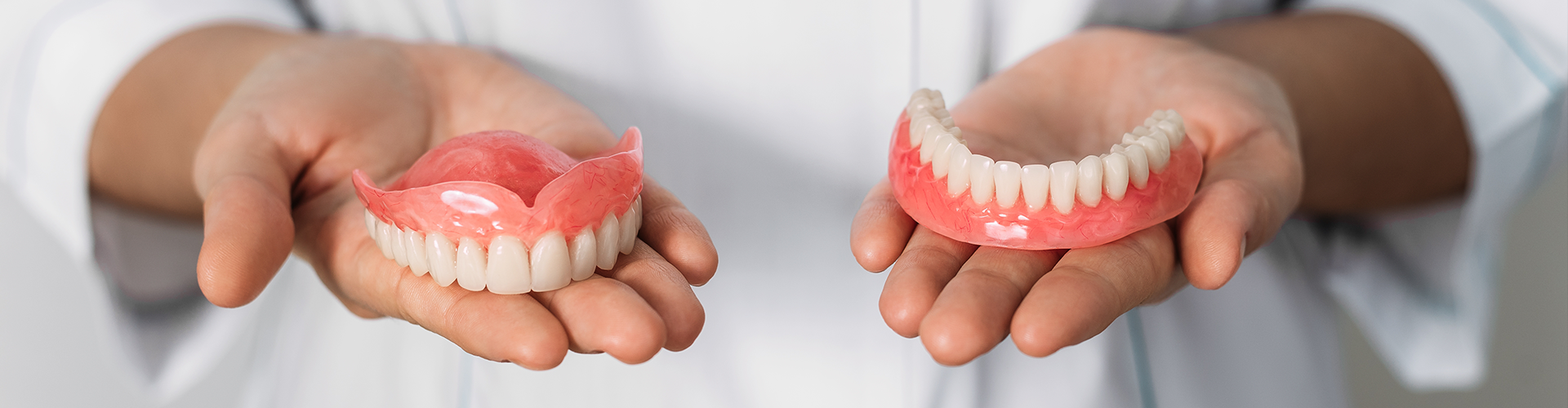 person holding upper denture in one hand and lower denture in the other hand