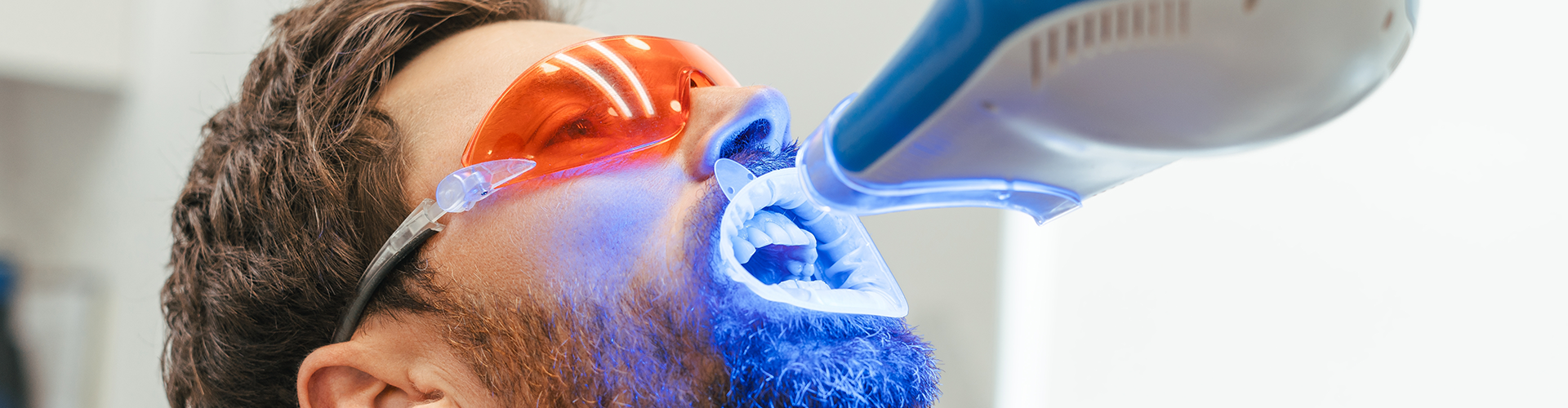 gloved hand shining light on the teeth of a man wearing orange glasses