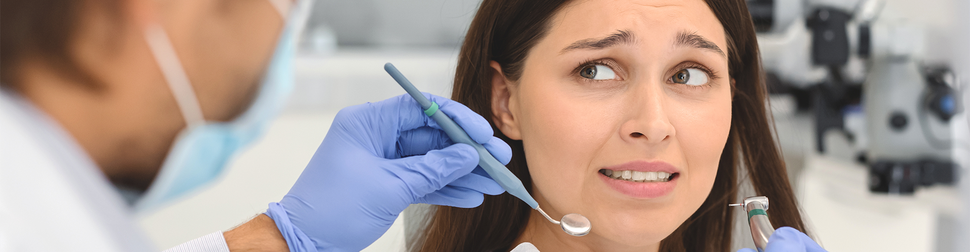 dentist holding dental tools towwards fearful-looking woman