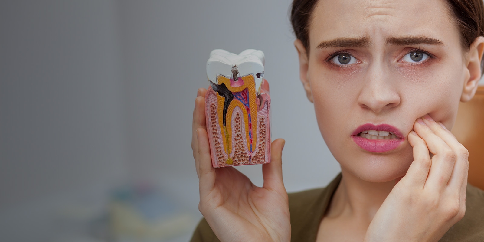 A woman holding a fake tooth while touching her cheek, showing toothache.