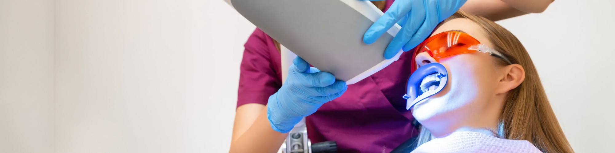 Dental-professional-shining-teeth-whitening-light-on-female-patient's-teeth.